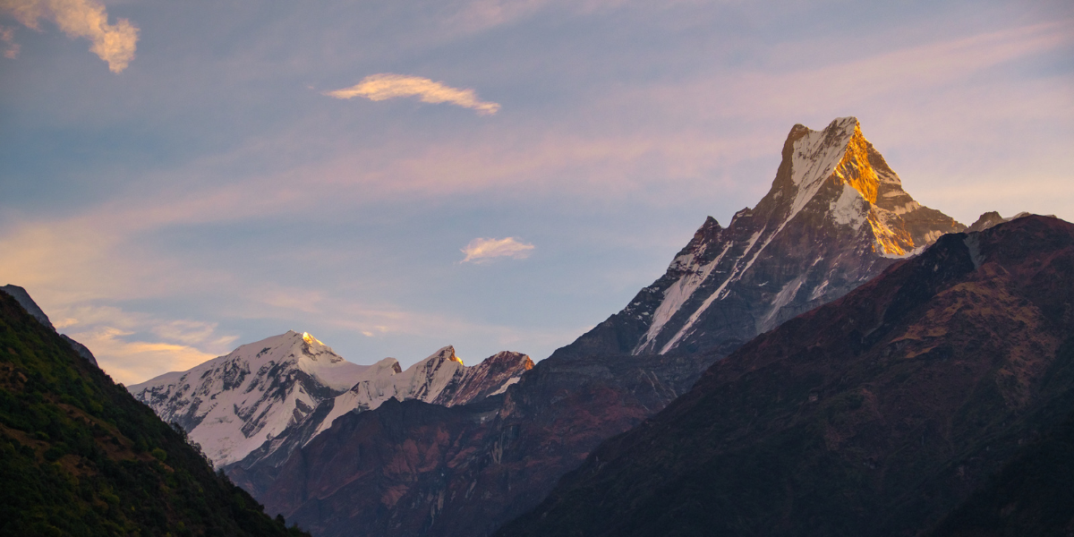 Mountain range with snow-capped peaks under a pink and blue sky.